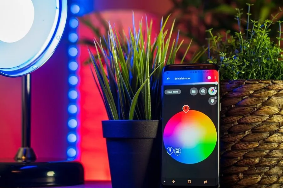 Celular mostrando seletor de cores de iluminação ao lado de luminária e fita de LED acesas em azul e vermelho