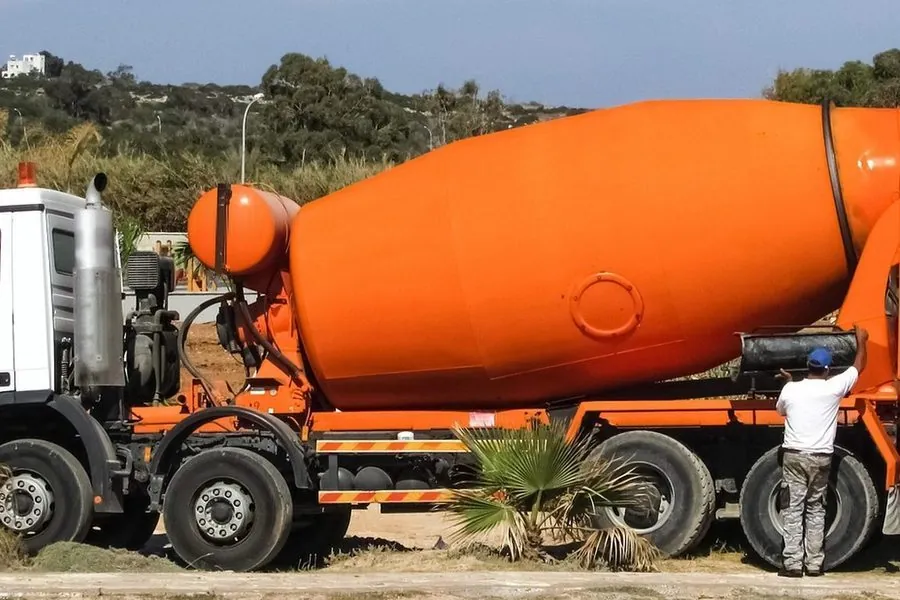Caminhão betoneira laranja estacionado no canteiro de obra, com um trabalhador ao lado da bica de descarga