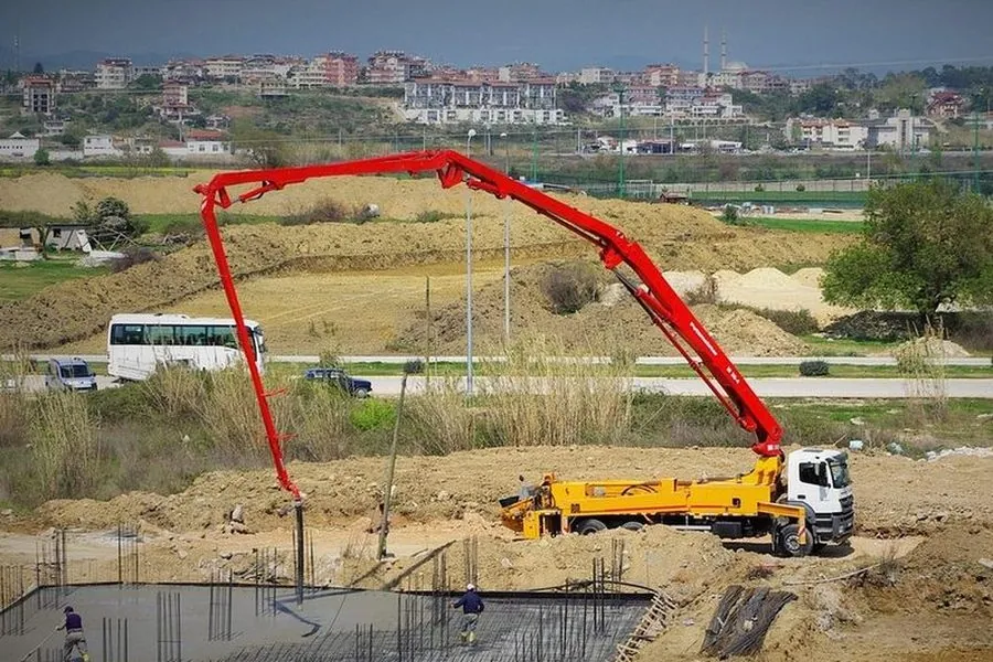 Caminhão com bomba lança vermelha estendida sobre a laje de uma obra em terreno aberto
